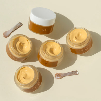 Five jars of a beige cream with a spoon on a beige background